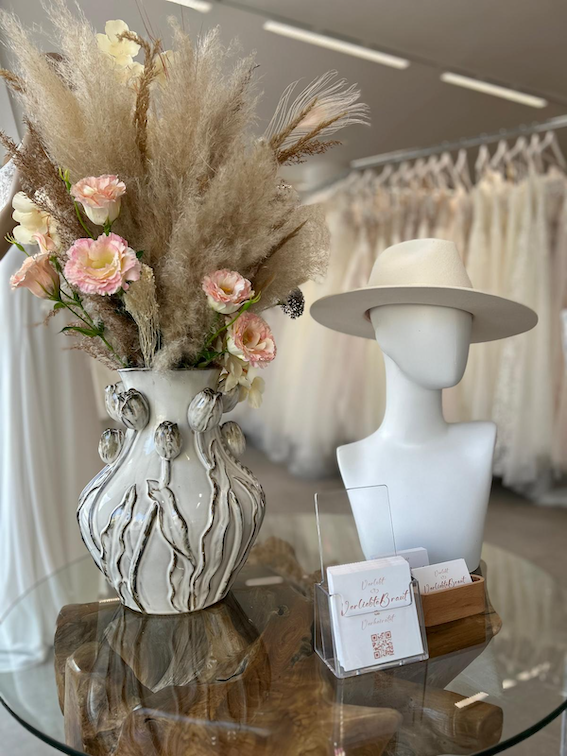 Eingangsbereich Vase mit Trockenblumen und Rosen neben einer weißen Schaufensterpuppe mit Hut.